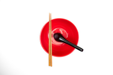 Red bowl with chopsticks and spoon on a white background. Top view