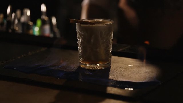 Bartender sets fire to cocktail, burning cinnamon in alcohol drink, barman makes drink.slow motion