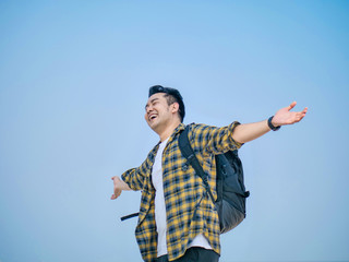 Happy Asian tourist with backpack raising his hands against the beach.