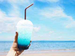 hand holding glass of Blue Hawaii drink with ice over summer beach background.