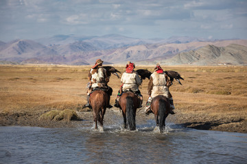 A group of traditional kazakh eagle hunters holding their golden eagles on horseback while walking...