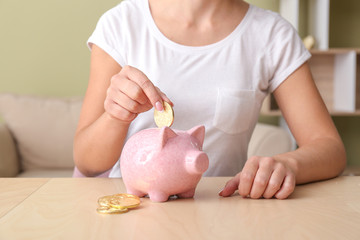 Obraz na płótnie Canvas Woman putting coin into piggy bank on table