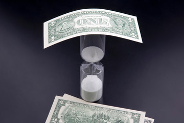 Dollar bills lie near the hourglass. Time is money. The salary. Business solutions in time....