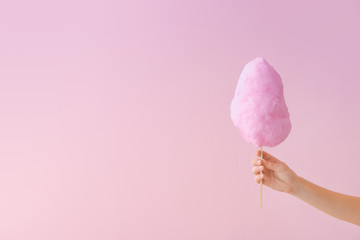 Female hand with tasty cotton candy on color background