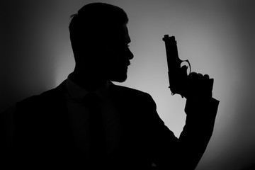 Silhouette of male agent with gun on dark background