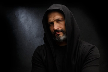 Fototapeta premium Portrait of a bald man with a beard in a black hood on a dirty gray background.