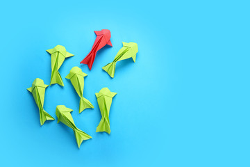 Red origami fish among green ones on color background. Concept of uniqueness