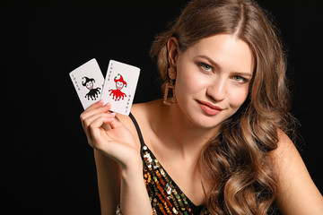 Beautiful young woman with playing cards on dark background