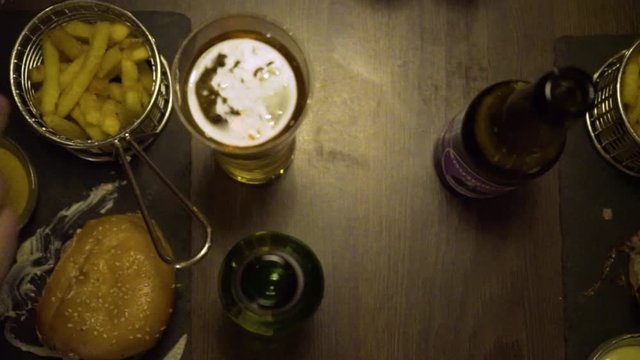 camera is sliding from right to left on top of a table with hamburgers and beer. French fries are standing on the table too