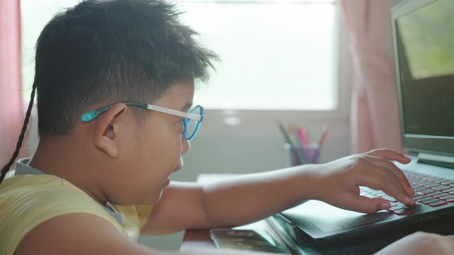 Close up of Happy Asian child boy wear eye glasses play games with laptops computer. Boy laugh, glad and happiness in a room that has sunlight from the window at home.