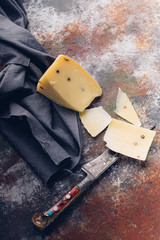Piece of Sheep cheese whit pepper and a knife on a rusty old background. Top view. Vertical shot