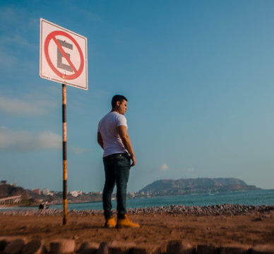 hombre parado mirando el altardecer al lado de una se&ntilde;al de trancito cielo azul
