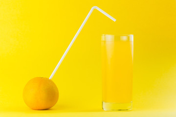 orange with straw next to a glass of orange juice isolated  on a orange colored background 