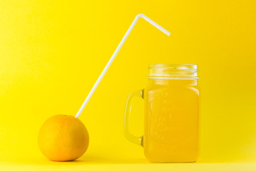orange with straw next to a jar of orange juice isolated  on a orange colored background with copy space 