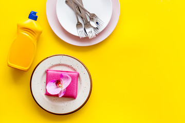 Dishwashing liquid bottle near plates on yellow background top view copy space