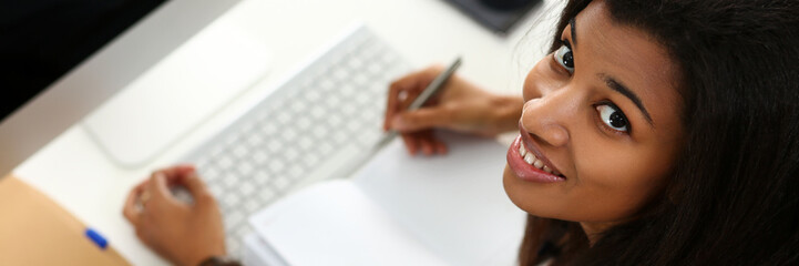 Black smiling woman sitting at workplace working with desktop pc