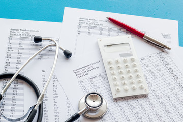 Health insurance concept. Stethoscope near financial documents and calculator on blue background