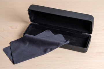 Dark blue case and cloth for cleaning glasses on a light wooden table. Eyeglass storage and care