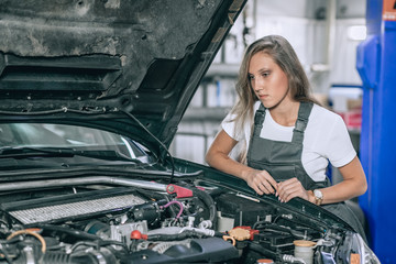 Fototapeta na wymiar Young woman from car service in a black jumpsuit and white t-shirt standing near the broken car. The girl opened the hood and looked at the engine. Refit woman car
