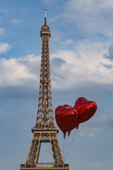 Heart shaped metallic red balloons in front of the eiffel tower with blue sky and some fluffy clouds