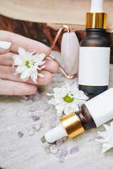 Fototapeta na wymiar Hand of woman talking blooming daisy flower and showing her rejuvenating natural serums and massage roller