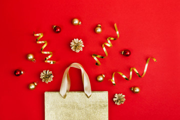 Golden Paper shopping bag, cones, serpanin and balls on red background. Christmas sale concept