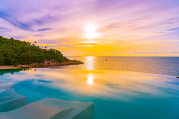 Fototapeta na wymiar Beautiful outdoor infinity swimming pool with coconut palm tree around beach sea ocean at sunrise or sunset time