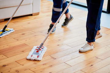 Closeup of janitors legs washing wooden floor with mops. Cleaning service concept