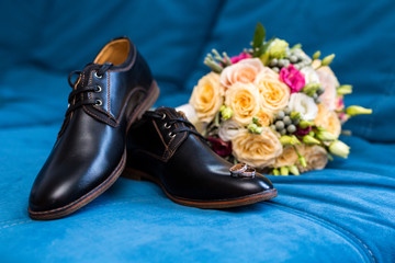 men's shoes wedding rings lie on men's shoes, next to a beautiful wedding bouquet on a blue...