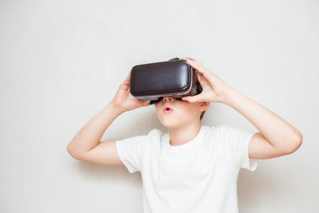 Happy teen boy wearing virtual reality goggles watching movies or playing video games, isolated on white. Cheerful teenager looking in VR glasses. Funny child experiencing 3D gadget technology