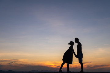 Silhouettes of happy young couple against the sunset sky.