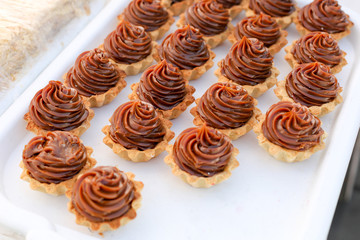 Many appetizing tartlets, cake basket with brown cream on a white tray. Summer dessert.