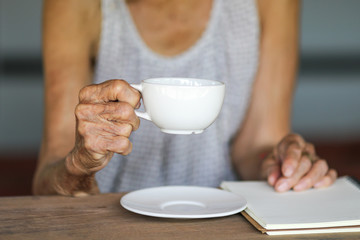Old asian woman with white coffee cup on wooden table