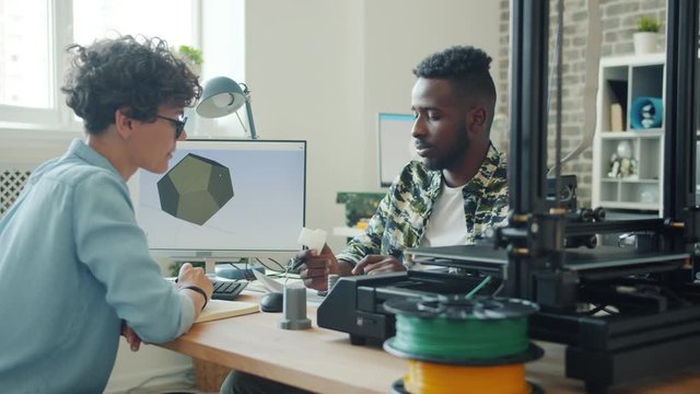 Creative designers man and woman are chatting in office holding 3d plastic models for printing sitting at desk using computer. People and innovation concept.