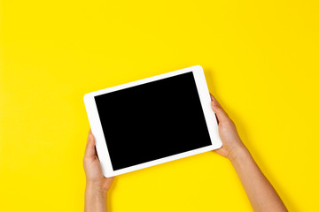 Kid hands holding white tablet computer on yellow background