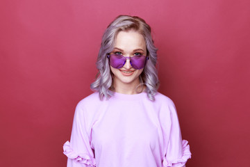 Portrait of young woman in bright glasses standing isolated over the pink background