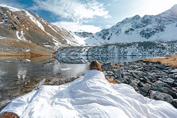 Young girl relaxing in comfy bed in wild nature with a view on beautiful landscape in winter