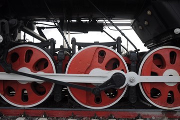 A row of red wheels of an old-fashioned steam locomotive with white levers and details.