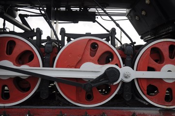 A row of red wheels of an old-fashioned steam locomotive with white levers and details.