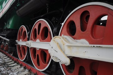 A row of red wheels of an old-fashioned steam locomotive with white levers and details.