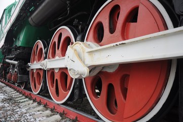A row of red wheels of an old-fashioned steam locomotive with white levers and details.