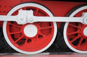 A row of red wheels of an old-fashioned steam locomotive with white levers and details.