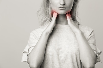 Female checking thyroid gland by herself. Close up of woman in white t- shirt touching neck with...