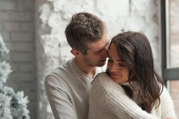Loving couple on a light background celebrates Christmas kissing each other. Love, cares, warmth.