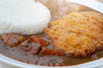 Tonkatsu, Japanese deep-fried pork cutlet on top with curry in white dish on wooden table. Japanese food.