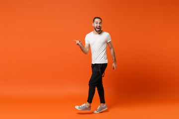 Excited young man in casual white t-shirt posing isolated on bright orange wall background studio...