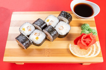 Sushi, rolls with cheese, crab and sweet potato. On the plank. On a red background.