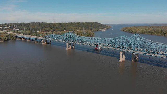 Drone footage of McClugage Bridge in Peoria, Illinois. A paddleboat slowly moves past the bridge