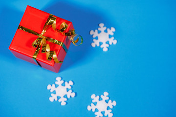 Gift, red box packed on a blue background with white snowflakes, close-up. Holiday, New Year, Christmas, surprise. Flat lay, top view, space for text.