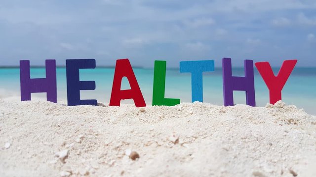 Static tripod shot of letters forming the word Healthy on a white sandy beach in Hawaii